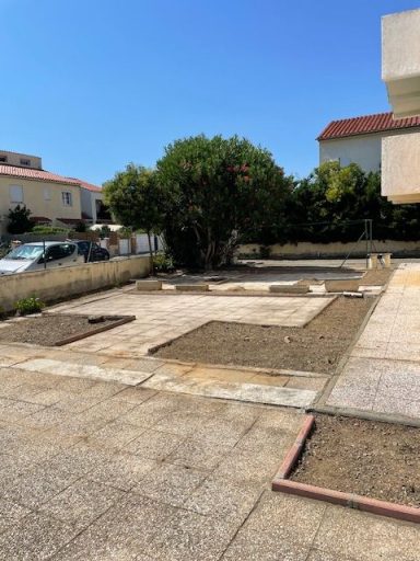 Terrain dégagé avec plusieurs parcelles en terre et un arbre au centre, ciel bleu.